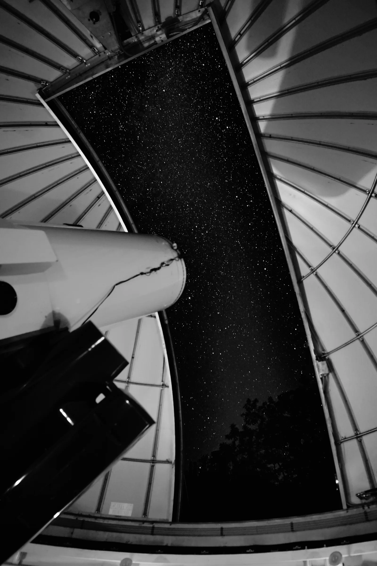 Looking up through the open slit of an observatory dome at a starry sky, with the telescope at left